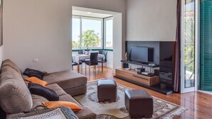 A modern living room with a sofa, ottoman, and a flat-screen TV on a wooden stand.