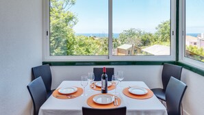 A dining table set for two with a view of the sea through a large window.