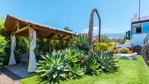 A patio with a thatched roof, surrounded by lush greenery and a well-maintained lawn.