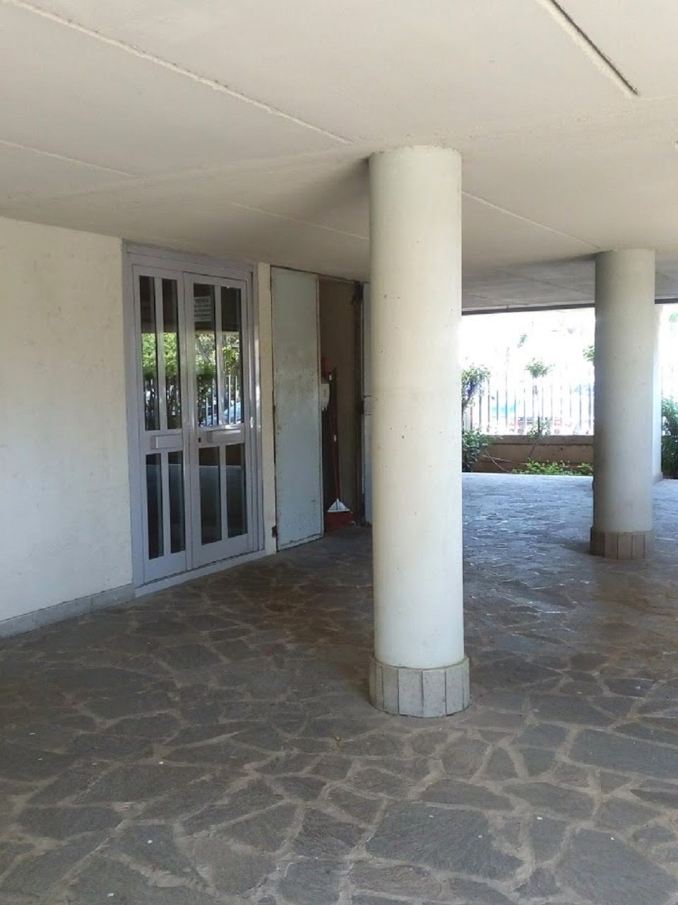 A covered outdoor area with stone flooring, white pillars, and a glass door leading to an interior space.