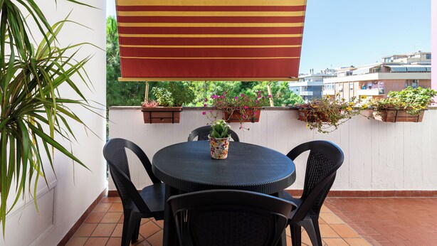 Une table ronde entourée de quatre chaises, un auvent rayé et des plantes en pot sur un balcon offrant une vue sur la ville.