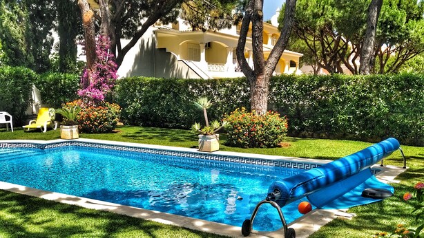 Une piscine avec un toboggan, entourée d’une végétation luxuriante et d’une pelouse bien entretenue.