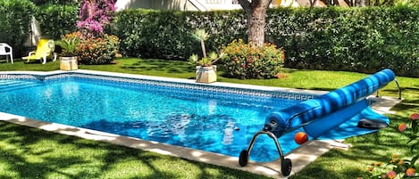 Una piscina con tobogán, rodeada de exuberante follaje y un césped bien cuidado.