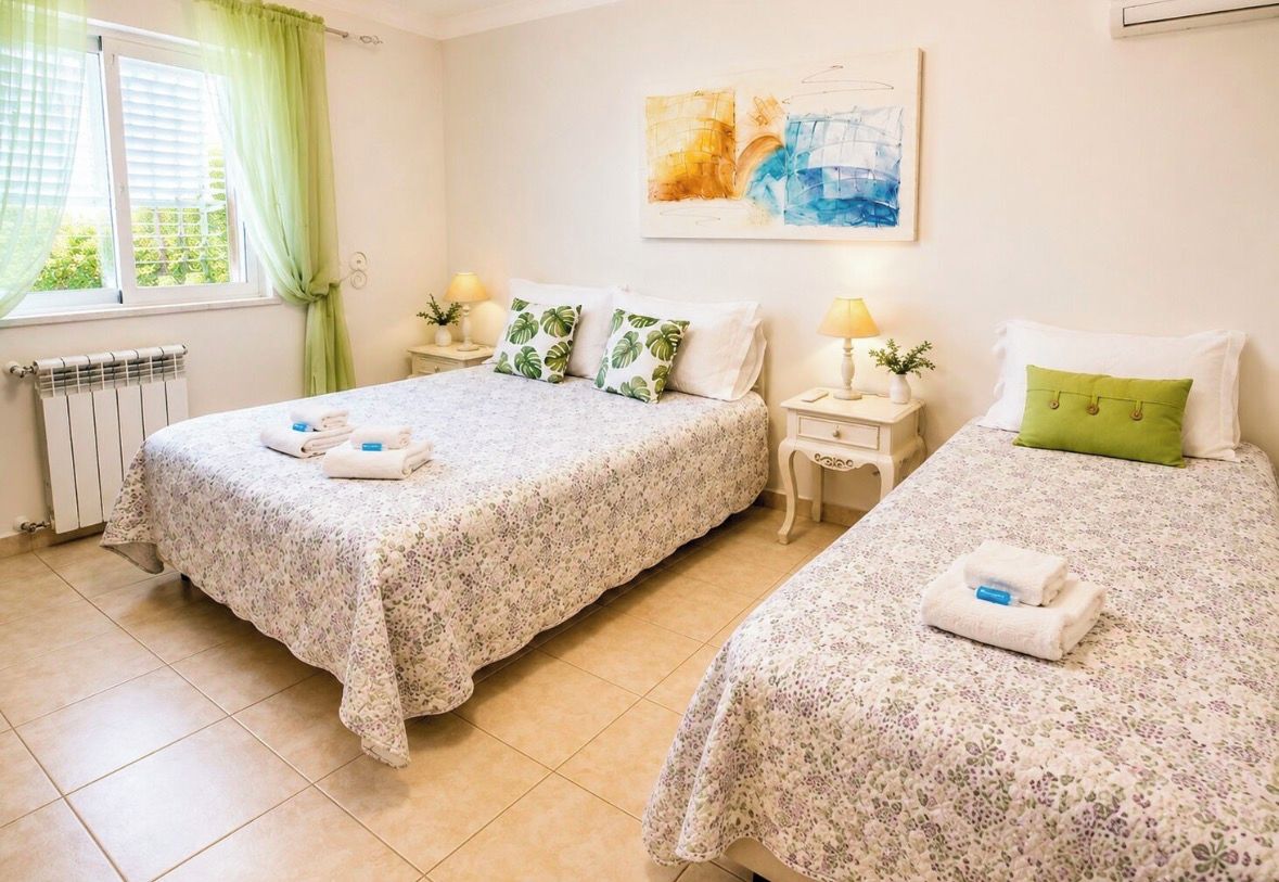 Une chambre d’hôtel avec deux lits, un radiateur, une fenêtre avec des rideaux, un tableau au mur et des lampes de chevet.