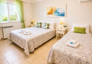Habitación de hotel con dos camas, un radiador, una ventana con cortinas, un cuadro en la pared y lámparas de noche.