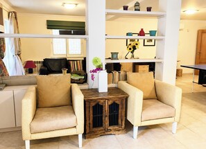 Een zithoek met twee beige fauteuils, een houten bijzettafeltje en een boekenkast met decoratieve objecten.