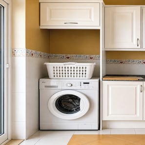 Un espacio de lavandería compacto con lavadora de carga frontal, tendedero y muebles de cocina blancos.