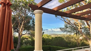 Un balcon agrémenté d’une pergola, d’une colonne et offrant une vue sur un paysage côtier.