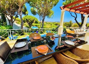 Un espace de restauration en plein air avec des tables disposées pour quatre personnes, entouré de meubles en osier, et offrant une vue sur une piscine et une végétation luxuriante.