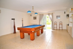 Een pooltafel in een ruimte met een betegelde vloer, een plafondventilator en twee barkrukken.