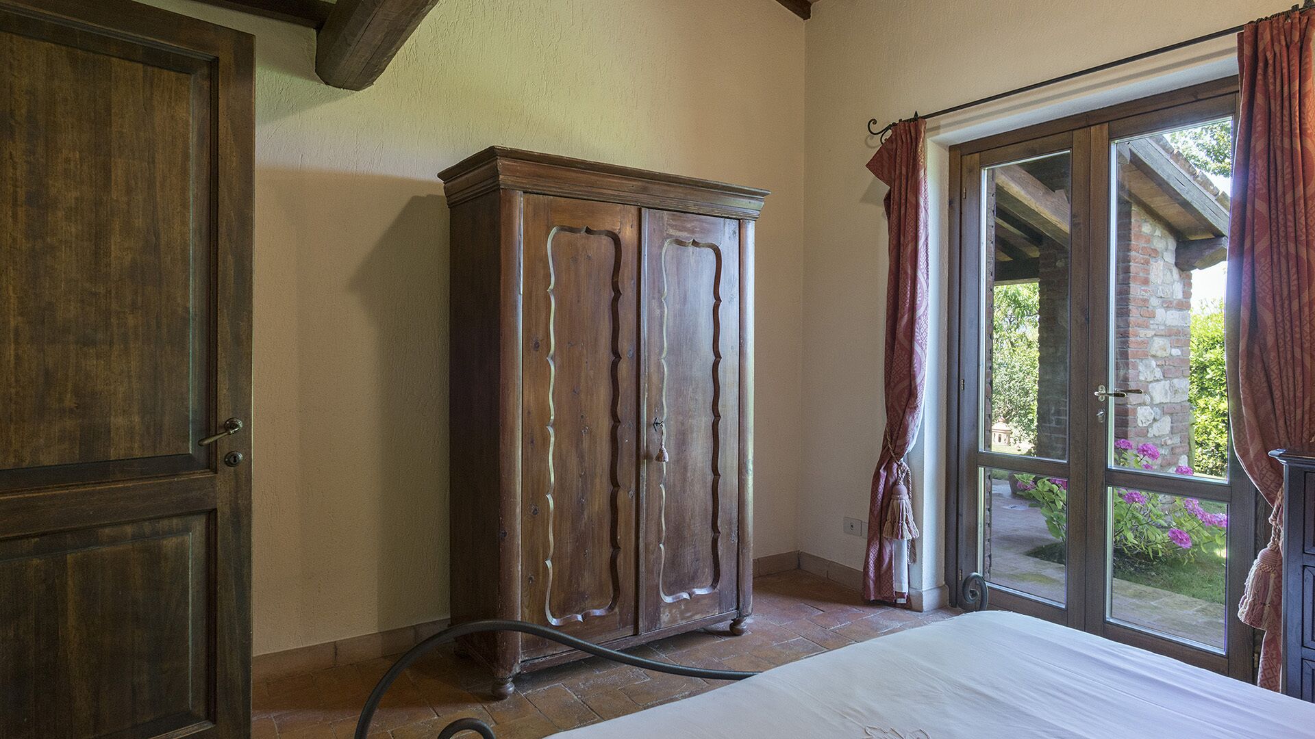 A room with a wooden wardrobe, a bed, and a window with curtains.