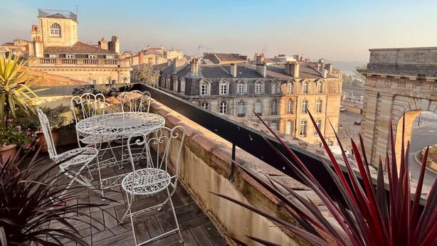 Una terrazza sul tetto con tavolo e sedie, affacciata su un panorama urbano con edifici storici.