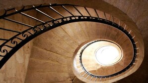 Una scala a chiocciola con ringhiera in metallo e un'apertura circolare in cima.