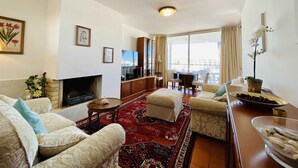 A spacious living room with a fireplace, comfortable seating, a television, and a large window offering a city view. - Exquisite one-bedroom apartment in Lagos Marina  (Lagos)