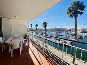 En balkon med udsigt over en lysthavn, hvide stole og et bord.