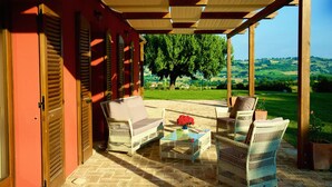 A covered patio with wicker furniture and a view of a green landscape.