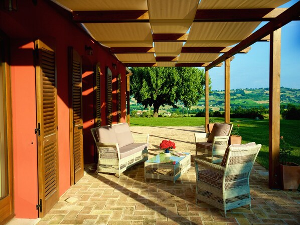 Eine überdachte Terrasse mit Korbmöbeln und Blick auf eine grüne Landschaft.