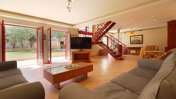Ein geräumiges Wohnzimmer mit großem Fernseher, einer Treppe und Blick ins Freie.