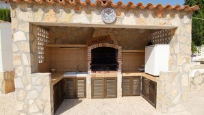 A stone-built outdoor kitchen with a 'BACARDI' sign, a built-in grill, and a white refrigerator. - 4 Bedroom villa, up to 10 people, Private pool & BBQ close to beaches and Calpe (Calpe)