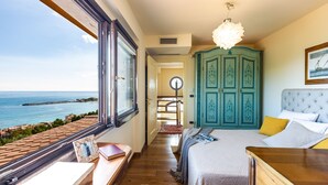 A bedroom with a large window overlooking the sea, a bed with a tufted headboard, a wooden desk, and a teal wardrobe. - Villa Alba 12, Emma Villas (Giardini Naxos)