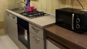 Cocina con estufa a gas, microondas y tostadora. Hay un lavamanos con grifo, un armario con manija y un enchufe de pared.