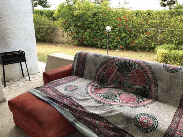 A patio area with a patterned sofa, a small table, and a grill.