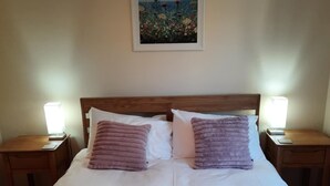A neatly made bed with two pillows, a painting on the wall, and bedside lamps.