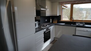 A modern kitchen with white cabinets, a built-in oven, a microwave, and a window with a view of trees.