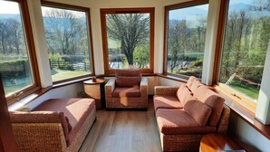 A cozy room with wicker furniture, large windows, and a view of a garden.