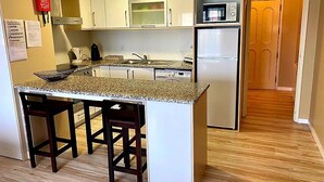 A compact kitchen with white cabinets, a granite countertop, a built-in microwave, and a refrigerator. There are two bar stools at the counter. - T2 by the beach, with pool, WIFI and cable TV, in Praia do Pedrogão (Coimbrão)