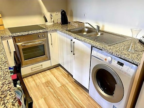 A compact kitchen with a built-in oven, a washing machine, and a sink.