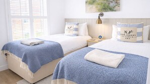 Hotelkamer met twee bedden, een raam met zonwering, een schilderij van een strand en kussens met de tekst 'N.J. New Jersey'.