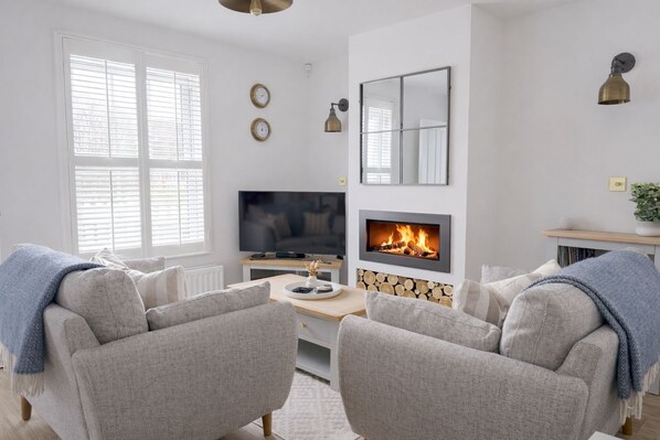 A modern living room with a fireplace, two armchairs, a TV, and a wooden table. - Escape to Beach Boutique: A Luxurious Haven in Camber Sands (Camber)