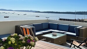 A deck with a blue sofa, wicker furniture, and a flower arrangement. Boats are visible on the water. - Waterfront duplex 150m2 12/14 pax, magnificent sea view. (Hyères)