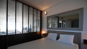 A hotel room with a large bed, a nightstand, a wall-mounted mirror, and a window with blinds. - Waterfront duplex 150m2 12/14 pax, magnificent sea view. (Hyères)