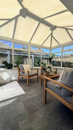 A sunroom with a high ceiling, large windows, and a view of the outside.