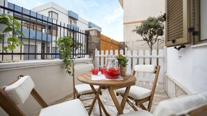 A small outdoor seating area with a round wooden table, four white cushioned chairs, and a pitcher of red drink. - Alghero Apartment Cervi 30 meters from Alghero beach for 6 persons (Alghero)