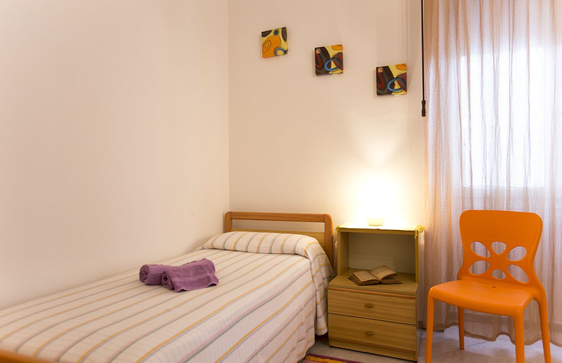 A bedroom with a bed, a nightstand, a chair, and artwork on the wall.