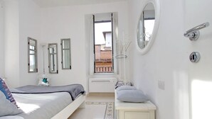 A bedroom with a bed, a bedside table, a mirror, and a window with a view of the outside.