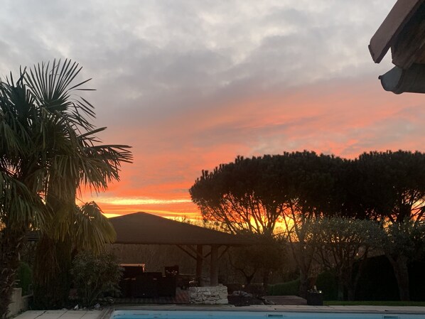 A pool area with a sunset view, surrounded by trees and a covered patio.
