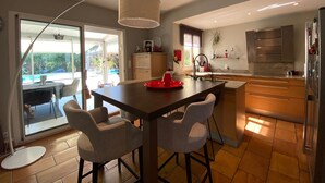 A modern kitchen with a central island, bar stools, a dining table, and a view of an outdoor pool. - Large air-conditioned house, swimming pool Secure Very quiet Pétanque, Table tennis (Saïx)