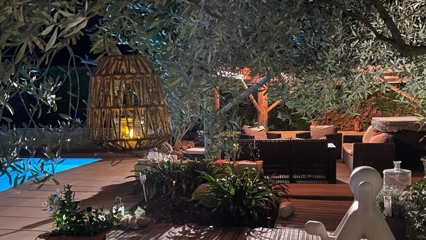 An outdoor patio area with wooden flooring, wicker furniture, and a decorative sculpture. - Large air-conditioned house, swimming pool Secure Very quiet Pétanque, Table tennis (Saïx)