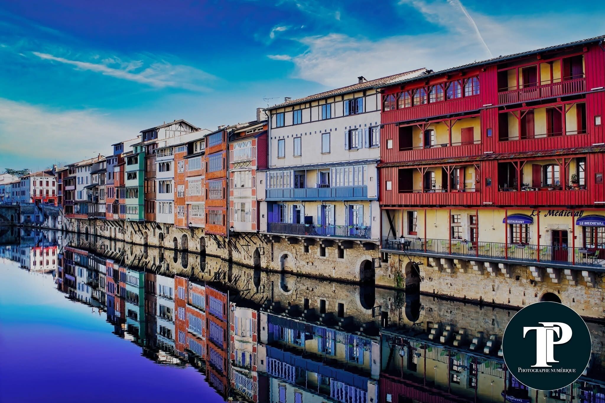 A row of colorful buildings along a canal with a clear reflection.