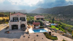 Uma casa de pedra de dois andares com piscina, rodeada por um jardim bem cuidado e com vista para uma paisagem montanhosa.