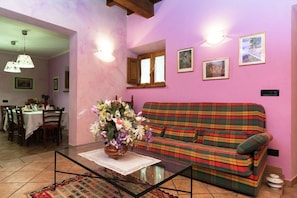 A living room with a plaid sofa, a glass coffee table with a vase of flowers, and a dining area with a table set for two.