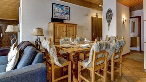A dining area with a wooden table set for four, surrounded by chairs with fur trim. A television is mounted on the wall above the table. - Penthouse 36 Savoleyres - La Tzoumaz, 4 Vallees (La Tzoumaz)