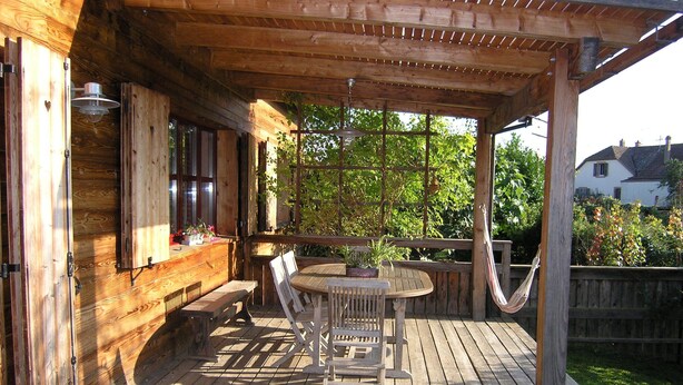 A wooden deck with a table and chairs, a hammock, and a pergola.