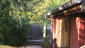 A wooden pathway leading to a red building with a tiled roof, surrounded by greenery and a wooden fence.
