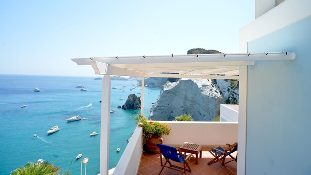 A balcony with a view of the sea and boats, a white pergola, and a potted plant.