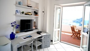 A modern room with a desk, TV, and a view of the beach through a glass door.